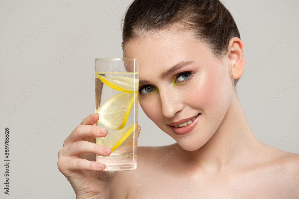 A healthy woman with clean skin holds a glass with water and lemon in her hand. Portrait of a cute young girl A healthy woman with clean skin holds a glass with water and lemon in her hand. Portrait of a cute young girl