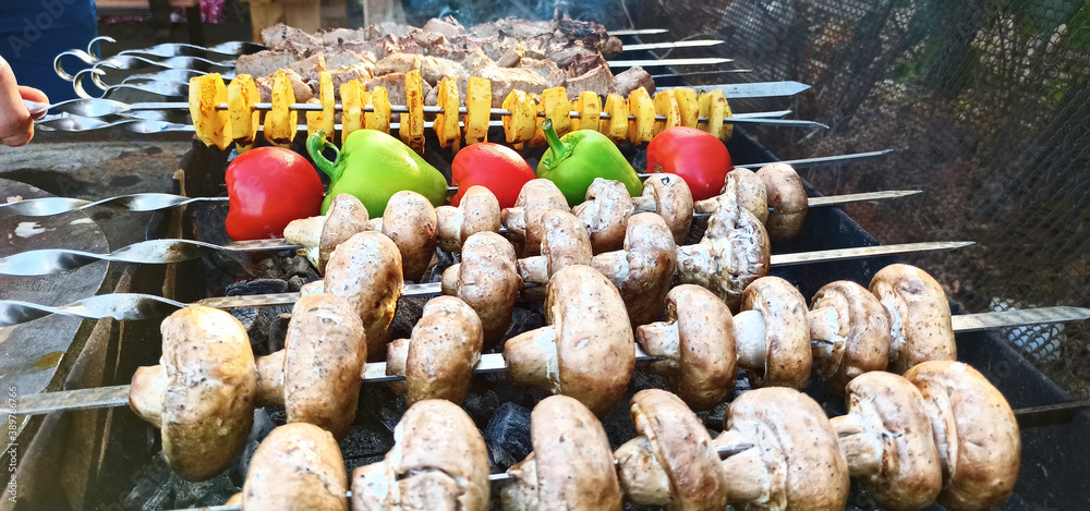 Close-up of pork shish kebab, vegetables and champignons outdoors with real charcoal, rustic style meat on the grill, barbecue.