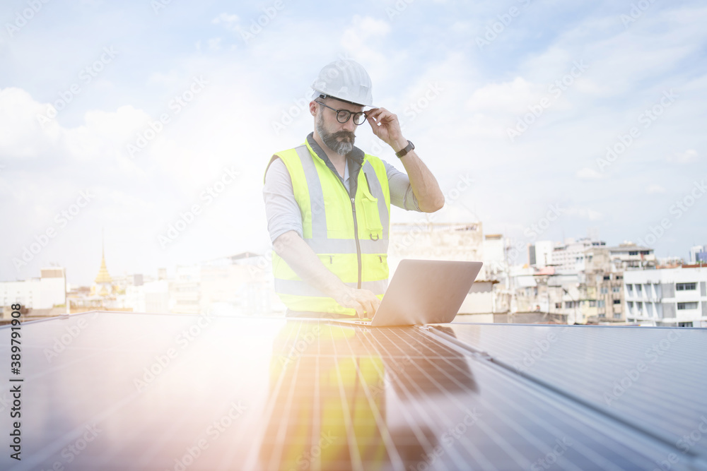 Rooftop solar power plant engineers sitting and examining photovoltaic panels. Concept of alternative energy and its service. Electrical and instrument technician use laptop to maintenance electric sy Rooftop solar power plant engineers sitting and examining photovoltaic panels. Concept of alternative energy and its service. Electrical and instrument technician use laptop to maintenance electric sy