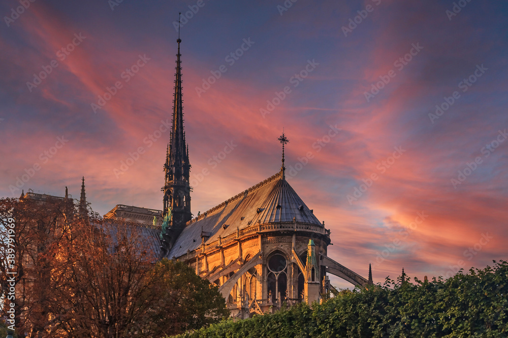 Details of the eastern facade of Notre Dame de Paris Cathedral facade with flying buttresses and ornate gothic spire in the warm light of sunset in Paris, France