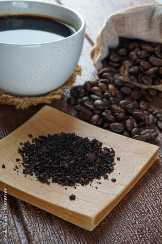 A cup of coffee, coffee beans and coffee powder on a wooden surface