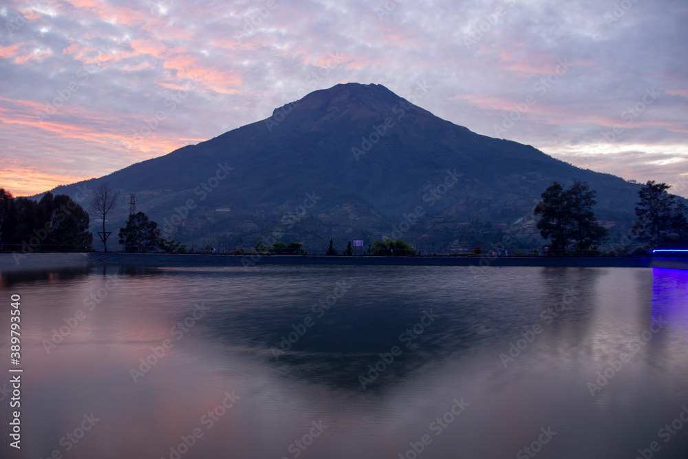 Embung Kledung is a tourist destination in Temanggung, Indonesia. a fish pond containing koi with a background of Sindoro mountain. clear sunrise sky with reflection on the artificial lake