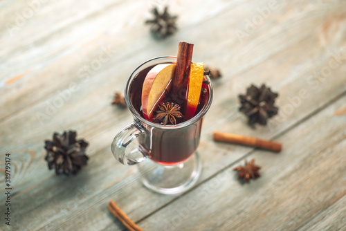 A glass cup with mulled wine decorated with cinnamon, star anise and fruit on a wooden table. Concept of a traditional hot winter beverage