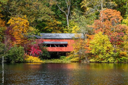Fototapet With beautiful reflections on Lake Loretta in Alley Park, Lancaster, Ohio, the red George Hutchins Covered Bridge, surrounded by colorful autumn leaves, was constructed in 1865 at another location