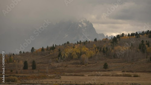 Timelapse of Aspen trees in distance during fall color and the Grand Teton range in the distance being taken over the storm.  National park in Wyoming during October in the fall season. 