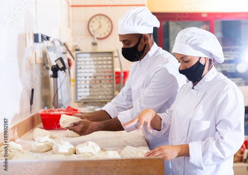 Male and female baker in protective mask working together in bakery shop