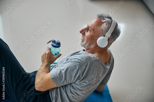 Active senior man in headphones smiling while resting from exercising