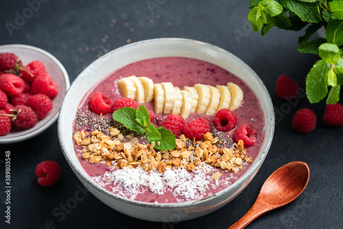 Pink smoothie bowl with raspberry, banana, granola and coconut on a black background, closeup view. Healthy vegan vegetarian detox smoothie bowl, superfood