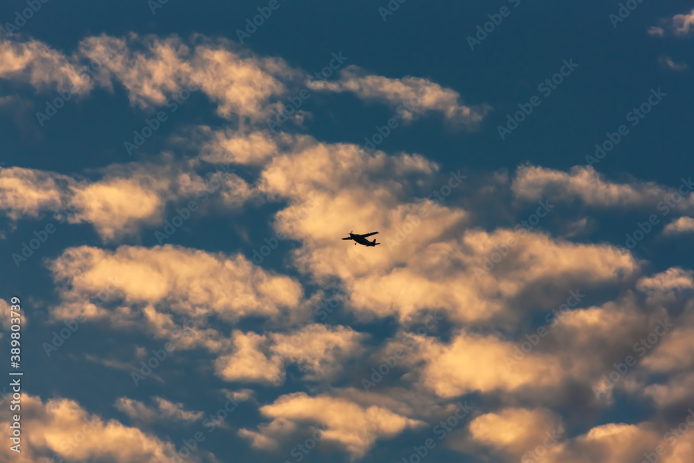 Blue sky with puffs of clouds and a small silhouette of an airplane