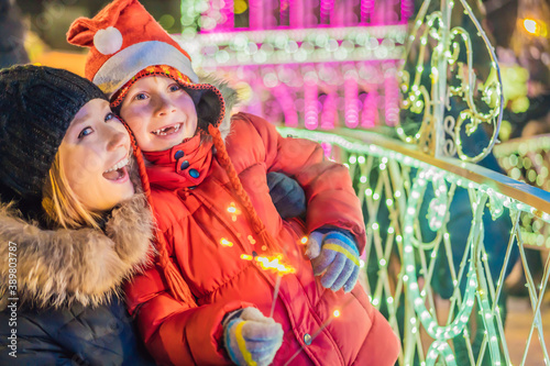Little boy and his mother with sparklers near giant fir tree and Christmas illumination on Christmas market. Xmas holidays on fair