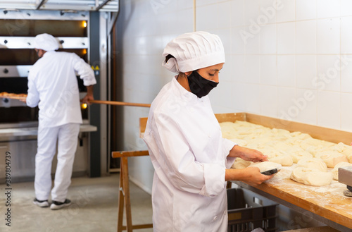 Bakery worker cuts raw dough with a knife