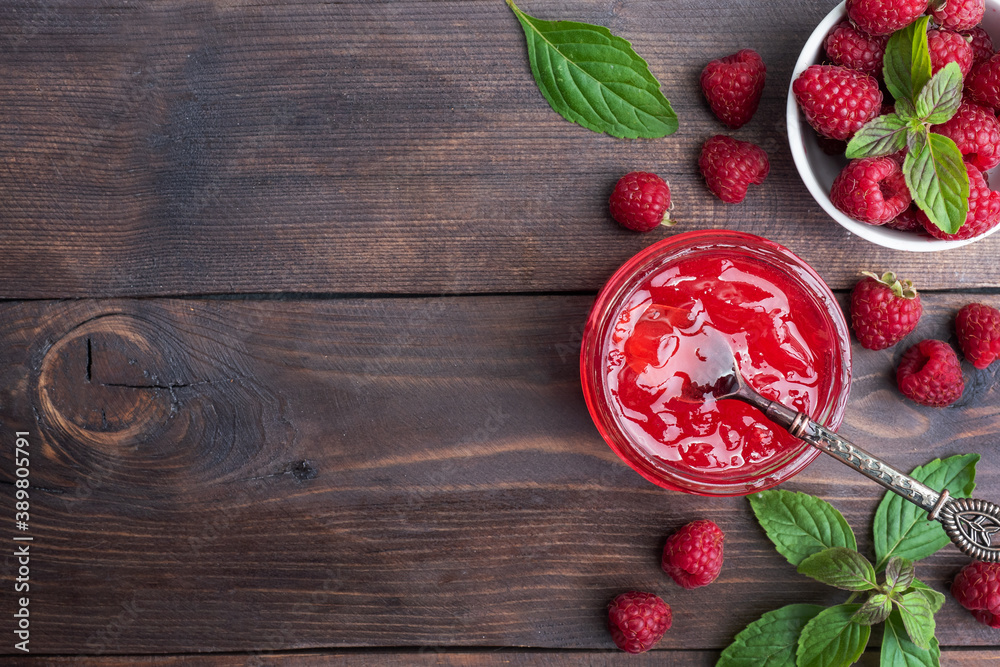 Homemade raspberry jam in a glass jar and fresh raspberries with mint on a wooden rustic background. Copy space Homemade raspberry jam in a glass jar and fresh raspberries with mint on a wooden rustic background. Copy space