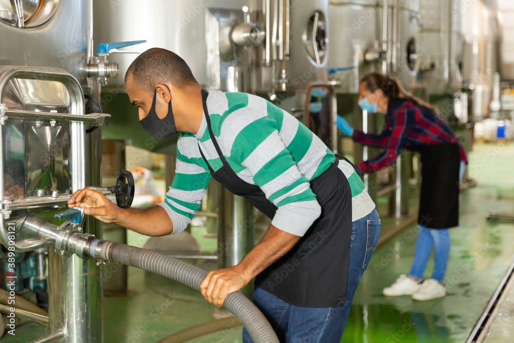 Working process at winery, man worker in protective mask working with fermentation tank