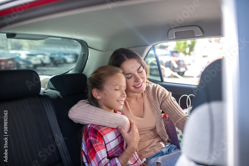 Mom hugging her daughter, sitting cheek to cheek on backseat of car