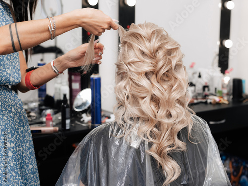Female hairdresser makes a festive hairstyle for a blonde in a beauty salon.