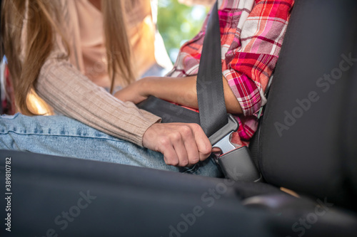 Close-up of female hands fastening girl's safety belt on backseat of car © zinkevych