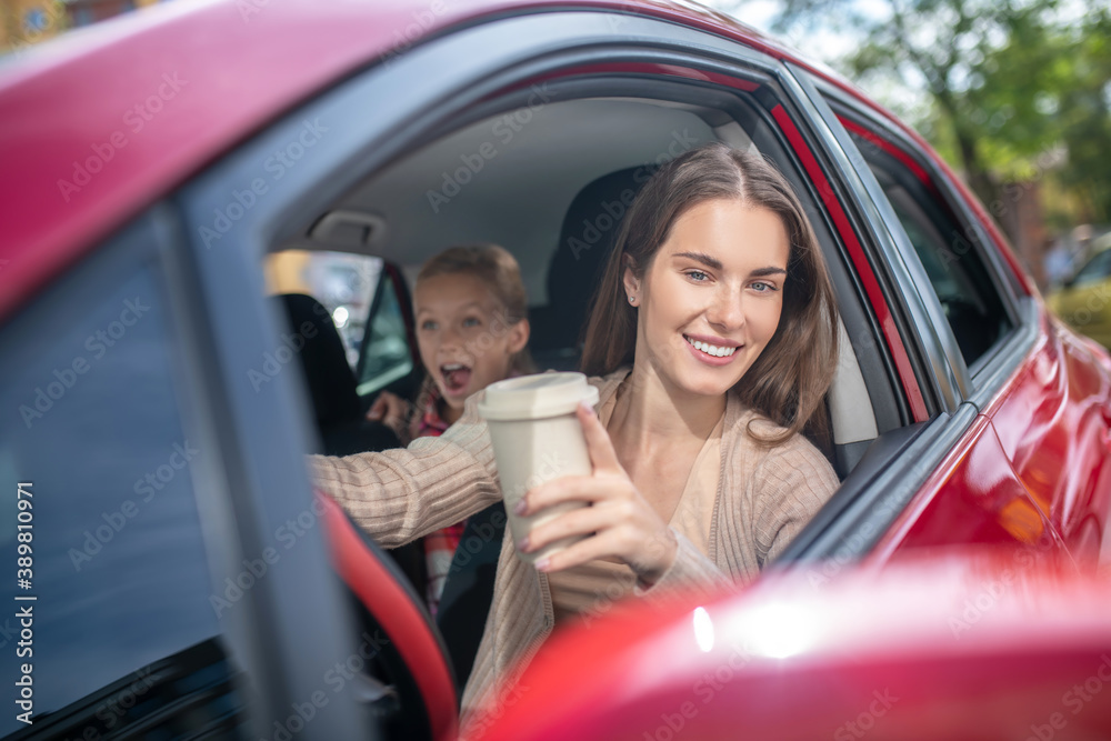Smiling mom holding coffee cup, driving with her amazed daughter
