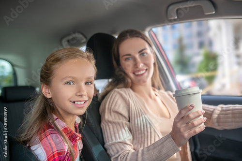 Smiling mom holding coffee cup, sitting in car with her daughter