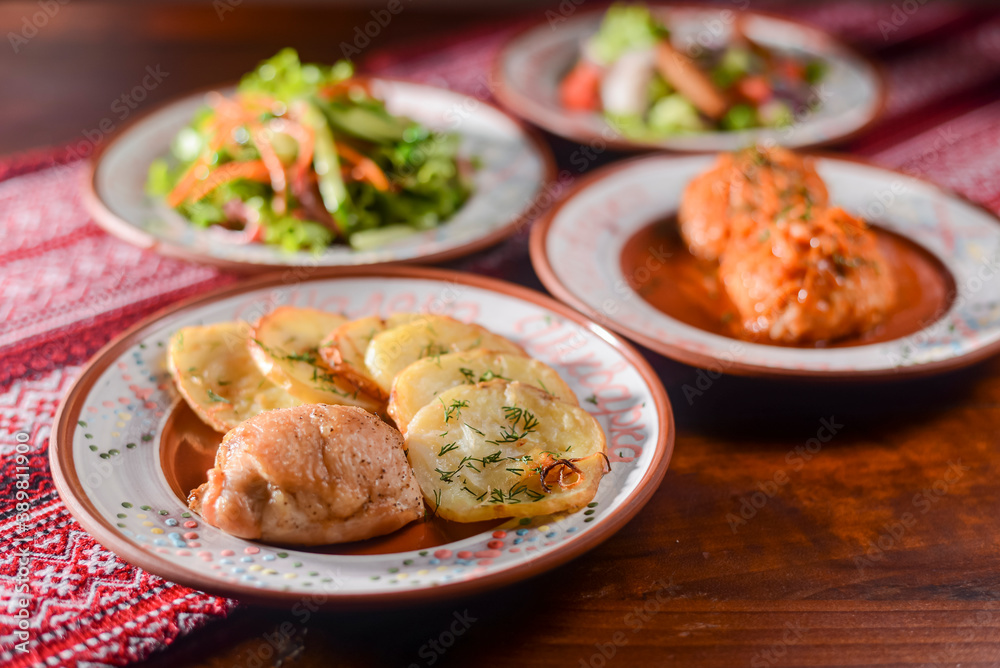 Traditional Ukrainian dishes in ceramic plates - baked potatoes, fried meat, fresh vegetable salad.