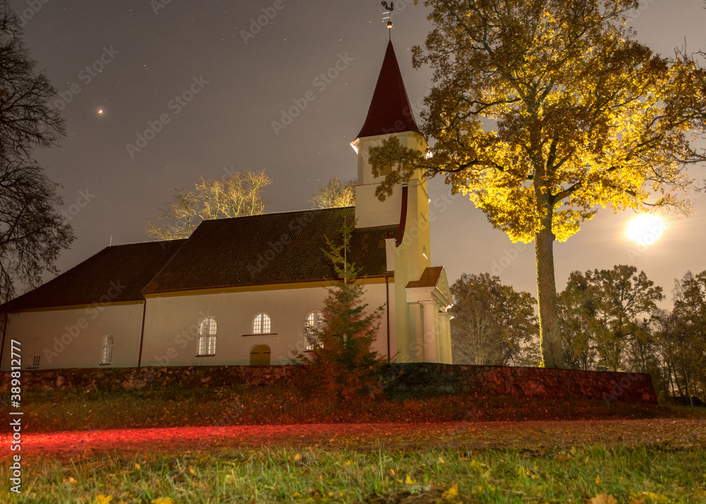 landscape with white church in the moonlight, illuminated tree in autumn colors at night