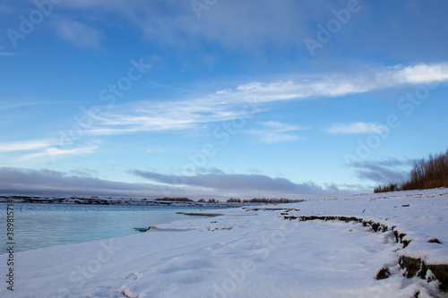 Freezing river. The river bank covered with snow and ice. Cold water under the blue sky.