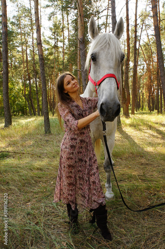 Beautiful girl in a sunny autumn forest walking with a white horse 