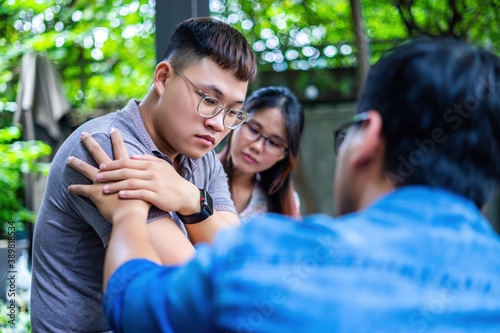 three asian friends sitting outside the office, over the shoulder view of a young Asian sad or stressed, his friends are comforting. photo