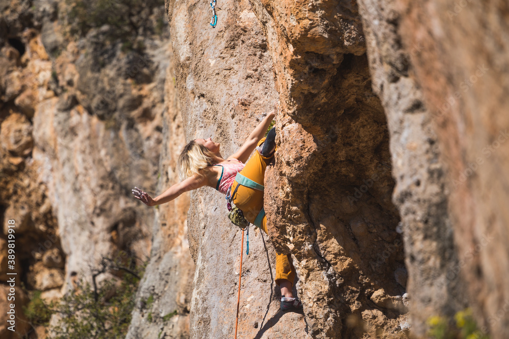 A strong woman climbs a beautiful orange rock.