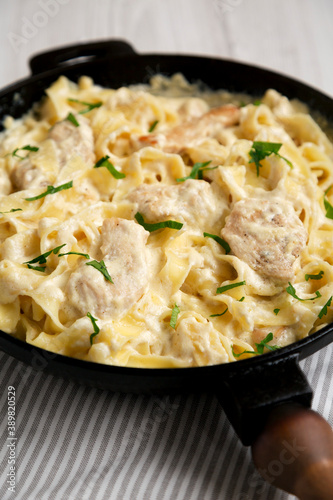 Homemade Chicken Fettuccine Alfredo in a cast-iron pan on a white wooden background, side view. Close-up.