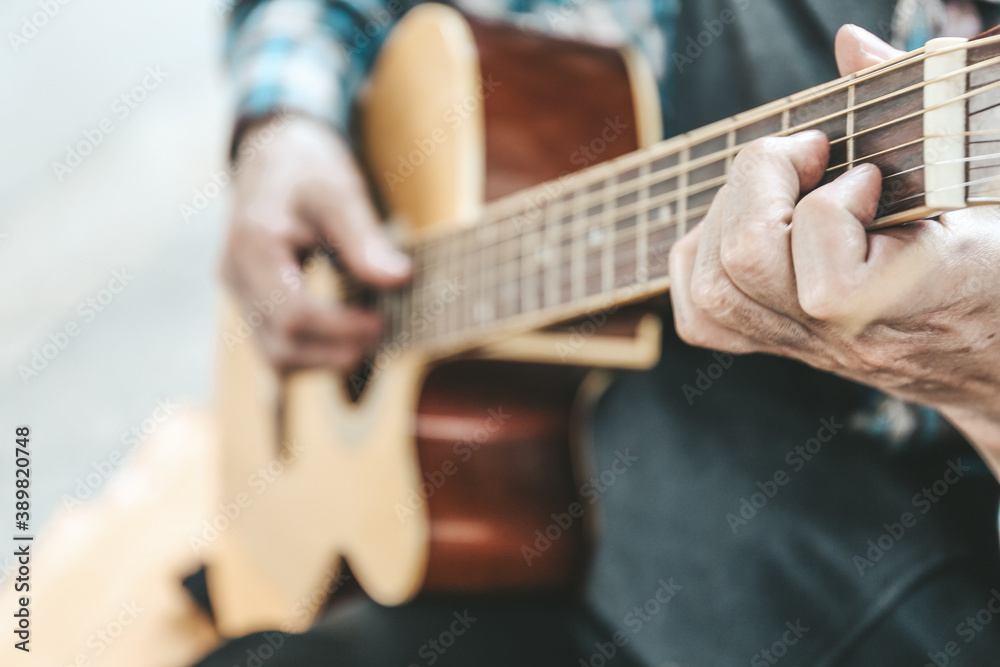 Senoir man sitting and playing acoustic guitar.