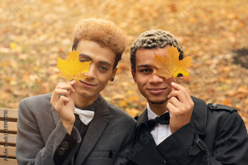 Young handsome black gay couple in love sitting on bench in park during autumn holding yellow leaves (selective focus). Concept of same sex love, equality and LGBT rights. Black lives matter!