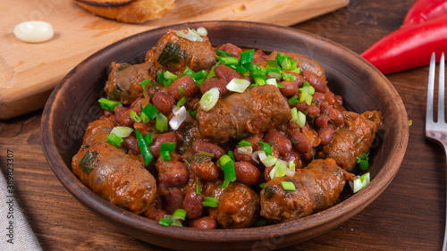 Traditional country Texas cowboy dish, beef sausages with beans, onions in tomato sauce in a rustic clay plate on a wooden table, close-up