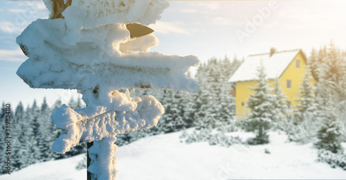 Snow covered signboards with wooden arrows on the background of house in the mountains. Winter travel concept 