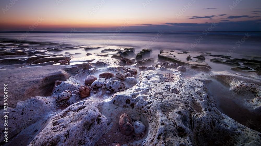 Obraz premium Calm ocean long exposure. Stones in mysterious mist of the sea waves. Concept of nature background. Sunset time on the beach. Sunlight on horizon. Balangan beach, Bali, Indonesia.