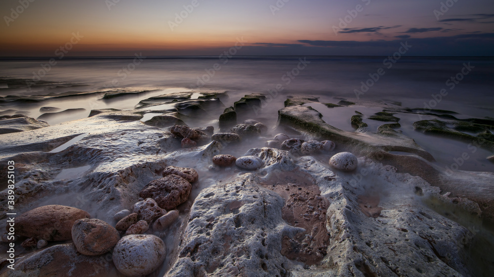 Obraz premium Calm ocean long exposure. Stones in mysterious mist of the sea waves. Concept of nature background. Sunset time on the beach. Sunlight on horizon. Balangan beach, Bali, Indonesia.