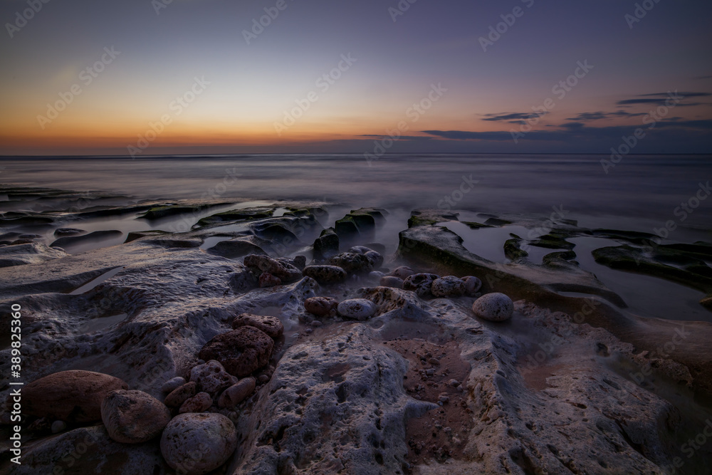 Obraz premium Calm ocean long exposure. Stones in mysterious mist of the sea waves. Concept of nature background. Sunset time on the beach. Sunlight on horizon. Balangan beach, Bali, Indonesia.