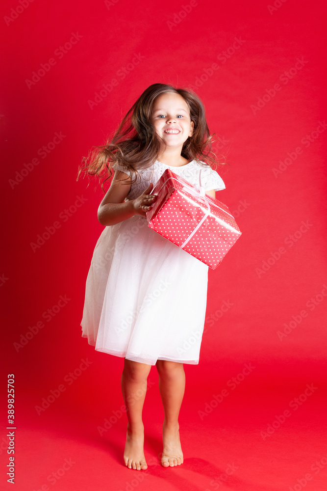 a fulllength girl in a white wedding dress jumps with happiness and holds a gift for Christmas or birthday on a scarlet background. a fulllength girl in a white wedding dress jumps with happiness and holds a gift for Christmas or birthday on a scarlet background.