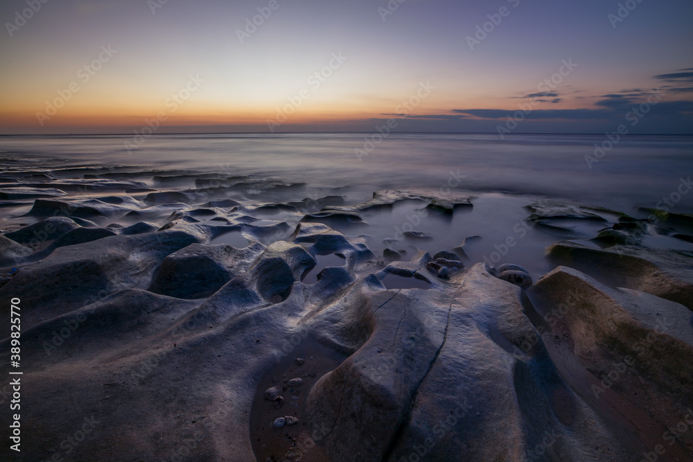 Calm ocean long exposure. Stones in mysterious mist of the sea waves. Concept of nature background. Sunset time on the beach. Sunlight on horizon. Balangan beach, Bali, Indonesia. Calm ocean long exposure. Stones in mysterious mist of the sea waves. Concept of nature background. Sunset time on the beach. Sunlight on horizon. Balangan beach, Bali, Indonesia.