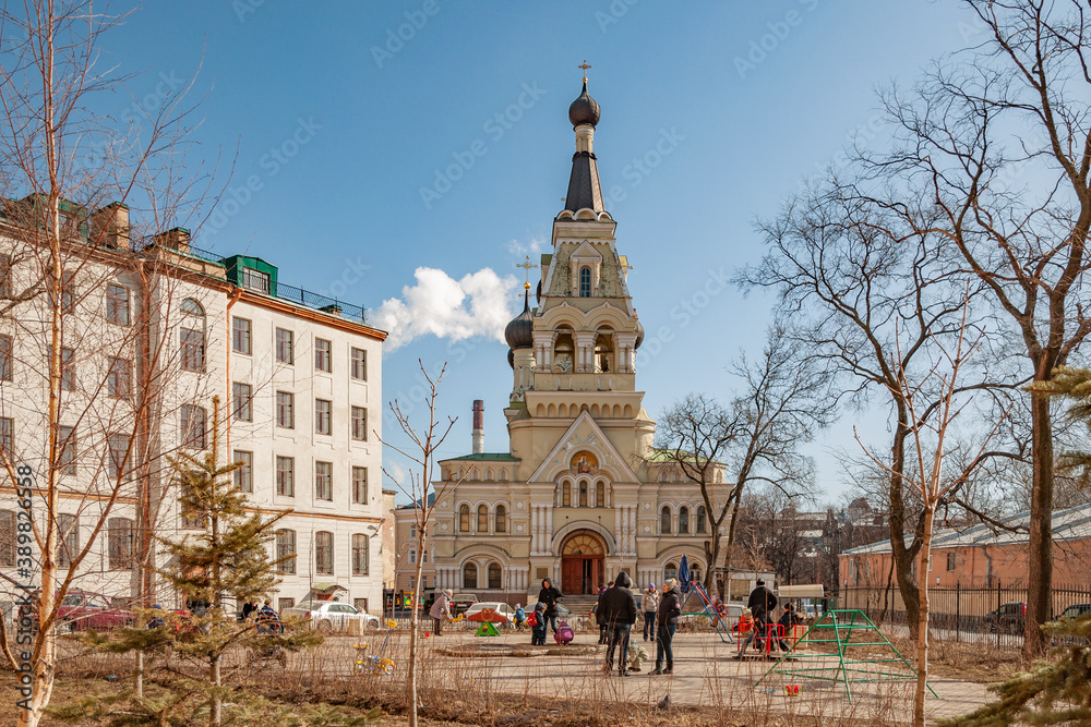 Obraz premium Bright, April, Sunday morning in the square against the background of the church and playground, where children play under the care of their parents
