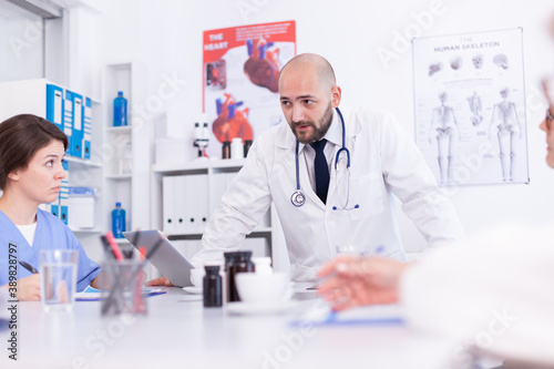 Expert doctor talking about medical technology with medical staff wearing lab coat. Clinic expert therapist talking with colleagues about disease, medicine professional.