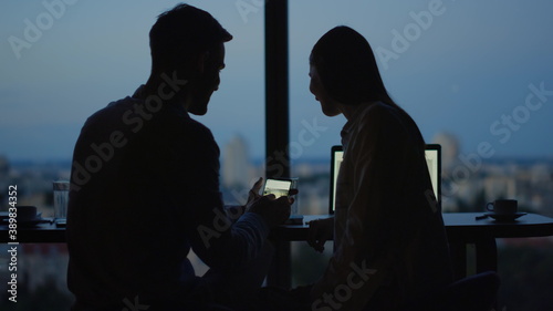 Silhouette of relaxed couple watching video on mobile phone in office.