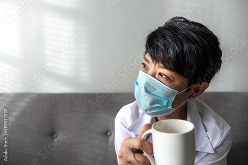 A lonely senior woman wearing a sanitary mark with a cup of coffee on her hand has been a lockdown at home due to coronavirus, or COVID-19 diseases. And Aged woman in depression sadness.