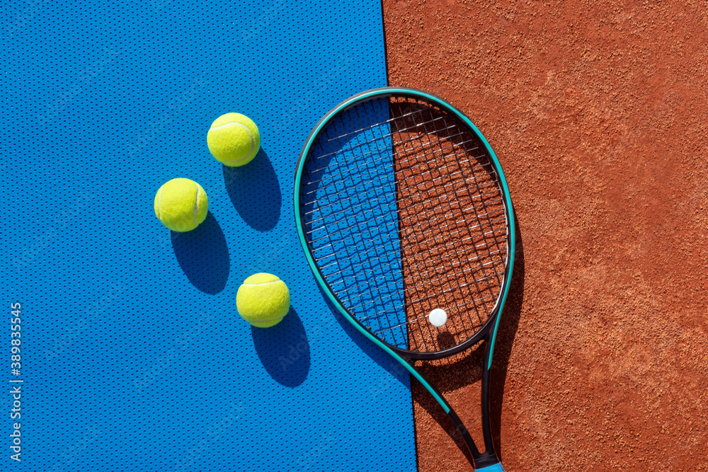 Tennis racket and balls on red clay court and blue gym mat. Funny concept of tennis, active games, leisure and healthy lifestyle. Sports background. Copy space for text
