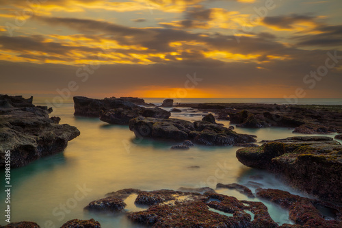 Beautiful seascape. Long exposure rocky beach during low tide. Panoramic ocean view. Composition of nature. Sunset scenery background. Cloudy sky. Water reflection. Mengening beach, Bali