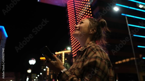 Happy lady using smartphone with beautiful bokeh in city vuilding background. Attractive young woman using smartphone standing on street of night town and takes picture photo