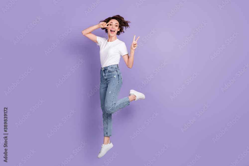 Full length body size photo of girl jumping high laughing showing peace v-sign gesture isolated on bright violet color background