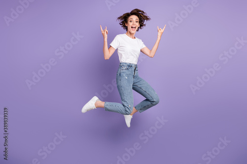 Full length body size photo of girl jumping high demonstrating heavy metal horns sign isolated on vibrant purple color background © deagreez