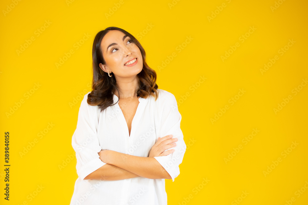 Portrait of a smiling young woman standing with arms folded and looking away at copy space isolated over yellow background Portrait of a smiling young woman standing with arms folded and looking away at copy space isolated over yellow background