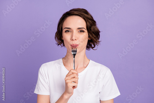 Portrait photo of slimming girl licking fork hungry diet wearing white t-shirt isolated on vibrant violet color background