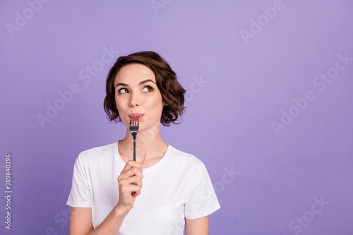 Portrait photo of dreamy girl licking fork thinking about diet looking at empty space isolated on bright purple color background
